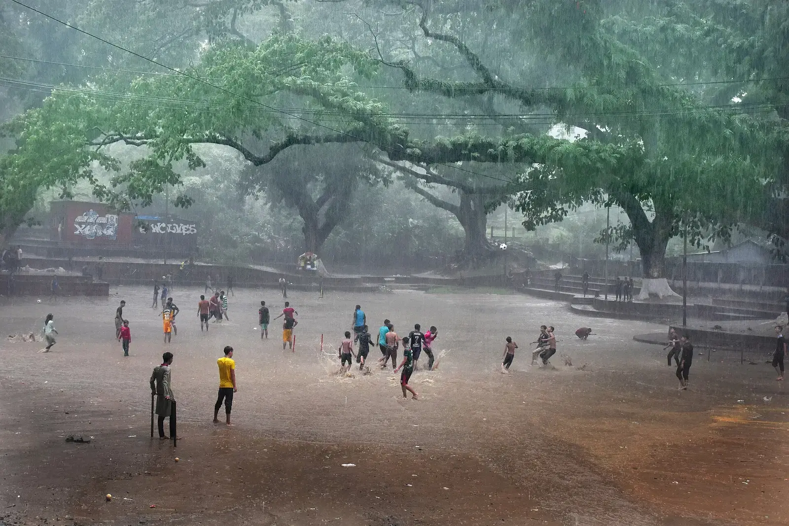 Children playing football in heavy monsoon rain on an open ground in Dhaka